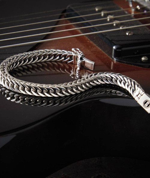32 Bar Blues A Little More Time, stainless steel chain necklace resting on a glossy black electric guitar with a brown body and metal strings.