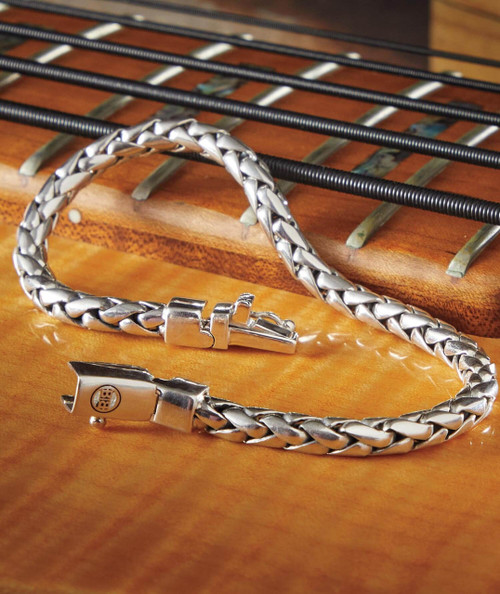 32 Bar Blues Bringin' The Hammer Down, close-up of a silver chain necklace with a clasp, placed on a wooden guitar fretboard.