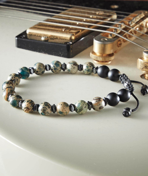 32 Bar Blues Let It Roll, beaded black, white, and camouflage-colored necklace with black beads, displayed on a light surface near a guitar.