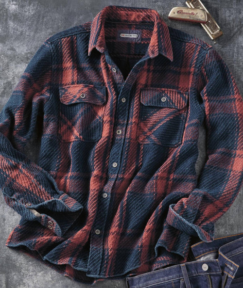 Remind Me, plaid flannel shirt with red and navy blue patterns, long sleeves, collar, and chest pockets, laying on a dark textured background with a pocketknife and denim jeans.