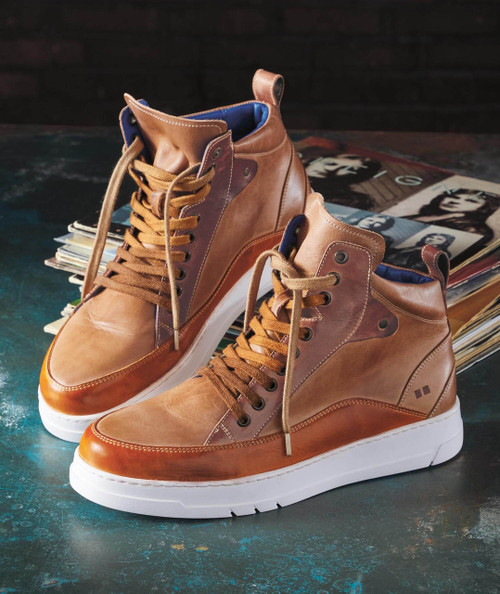 Ground Hog, stylish high-top leather sneakers with white soles and brown laces, on a dark textured surface with magazines in the background.