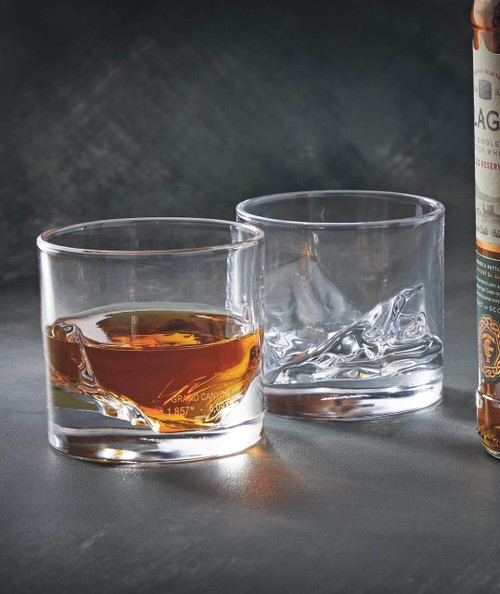 Boogie Woogie Cocktail, two clear glass tumblers with one filled with whiskey and ice, and the other empty, against a dark textured background.