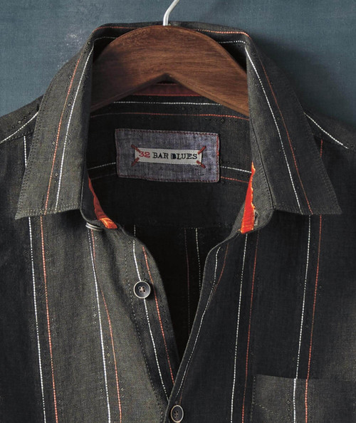 Soul Deep, close-up of a black striped shirt with red, white, and gray lines, hanging on a wooden hanger.