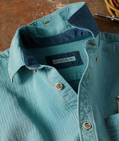 Swingline, a men's button-down casual shirt in light blue with darker blue accents on the inner collar and buttonholes, laid flat on a wooden surface.