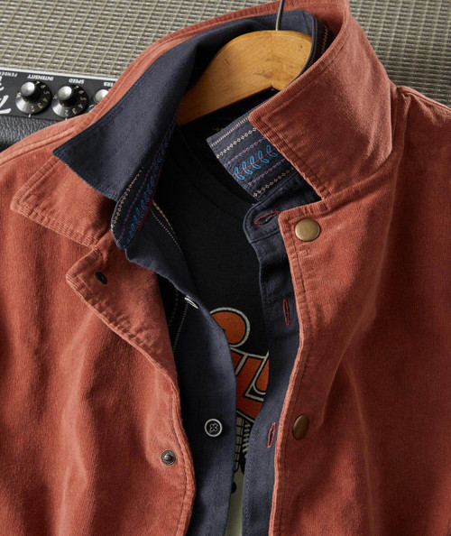 I'm Gonna Win product, close-up of a stylish layered casual outfit with a rust-colored jacket, dark inner shirt, and a black T-shirt with a graphic print.
