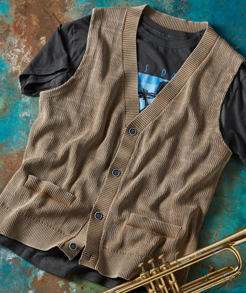 Centerpiece, a brown and black cardigan sweater layered over a t-shirt with a guitar graphic, placed on a textured, colorful background with a brass trumpet at the corner.