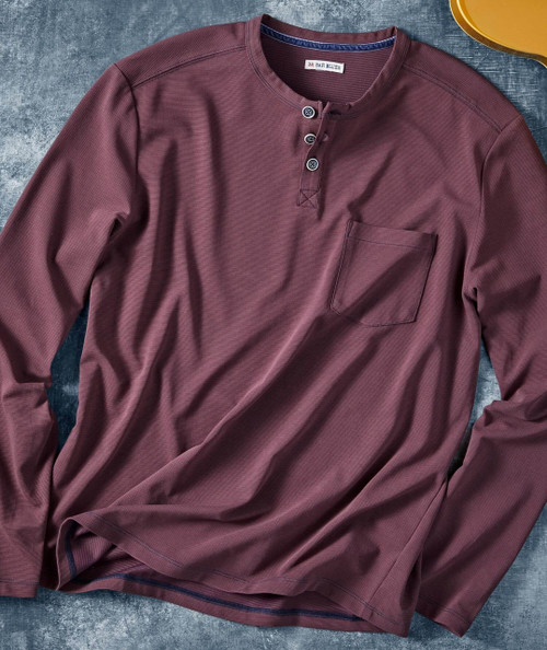 Rhythm Sundae, close-up of a maroon long-sleeve Henley shirt with a single chest pocket and a few buttons at the collar area, laid on a textured surface.