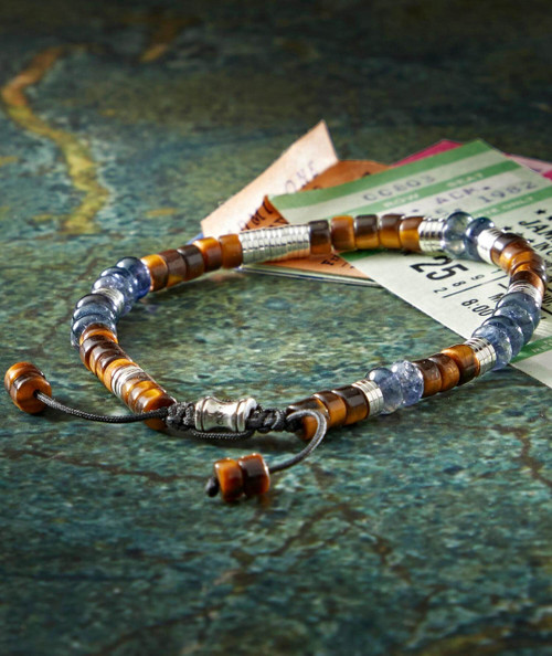 Bopity Bop, beaded jewelry bracelet with brown and silver beads placed on a green textured surface, alongside event tickets and paper currency.