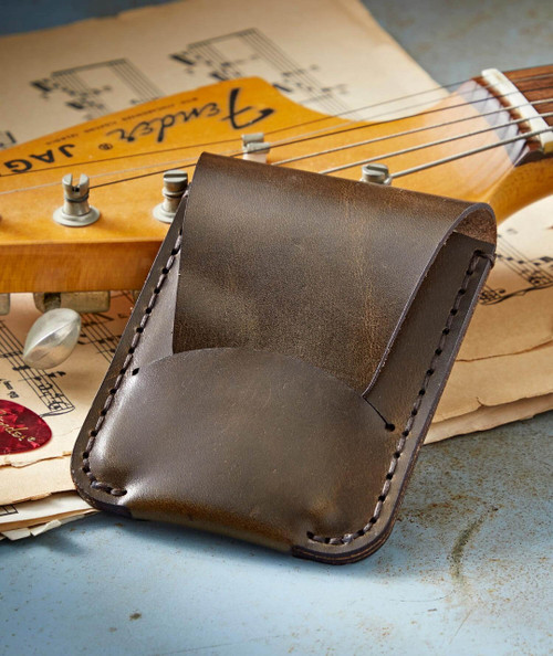 Put It Away, leather guitar pick holder with a quarter pocket on top of vintage sheet music and a guitar headstock.