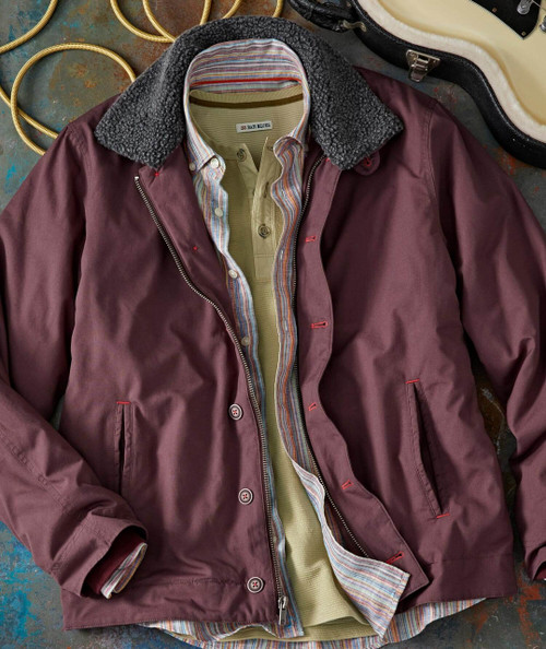 Cut The Deck, men's layered outfit with maroon jacket over a striped shirt and beige pullover, laid out flat on a textured surface with a guitar case and coiled cables in the background.