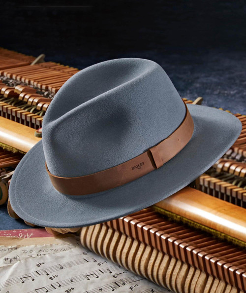 Decidedly stylish blue felt fedora hat with a brown leather band, placed on a wooden xylophone with sheet music underneath, ideal for fashionable accessories.