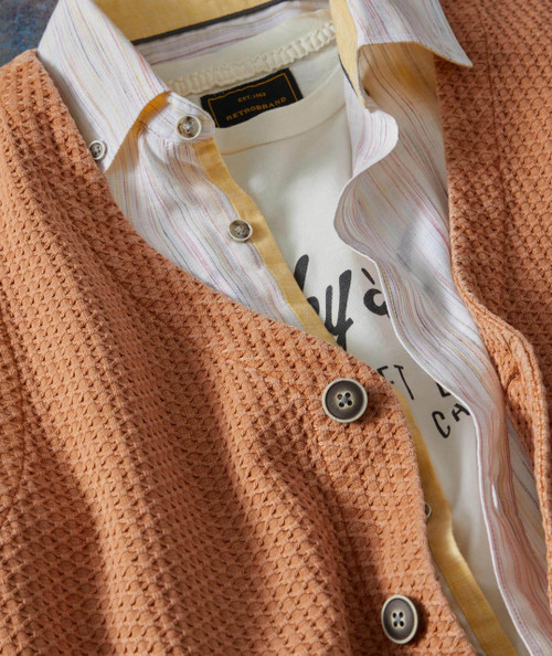 Diamonds And Rust, close-up of layered clothing with a textured peach-colored cardigan, a striped button-up shirt, and a printed T-shirt.