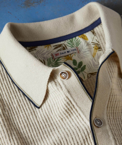 Cast Away, close-up image of a beige collared shirt with a textured ribbed pattern, featuring white buttons and a navy blue trim on the collar and placket.