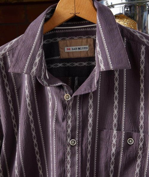 Twist And Shake, close-up image of a stylish, textured purple button-up shirt on a hanger.