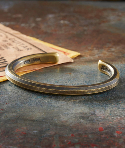 Chang Chang Chang, metallic cuff bracelet with engraved details resting on a textured surface near vintage papers.