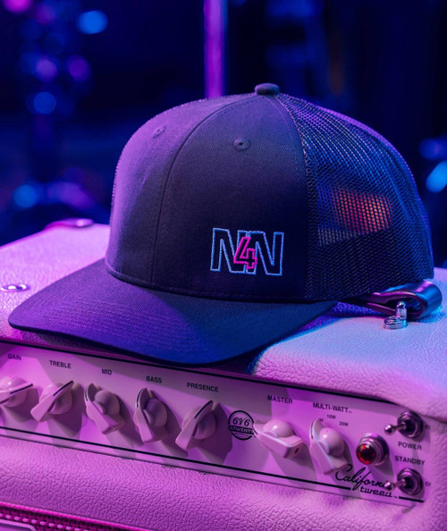 This Note's For You, a black baseball cap with embroidered 'N4N' logo, is placed on a musical amplifier under colorful stage lighting.