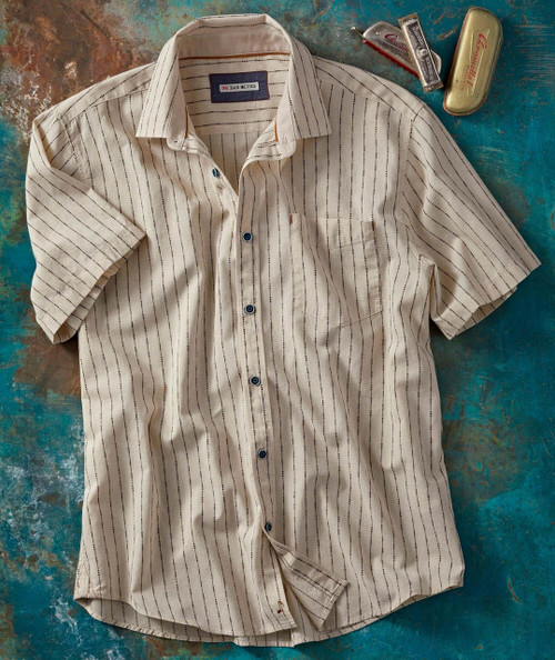 The Jitter Jump, a striped short-sleeve shirt with a pocket and buttons, laid flat on a textured surface with cigar boxes and a harmonica.