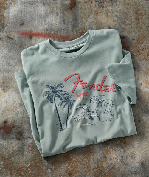 The Beast, vintage-style unisex T-shirt featuring palm trees and ocean waves, with red and blue Fender logo and 'Since 1946' text, laid on a distressed concrete surface.