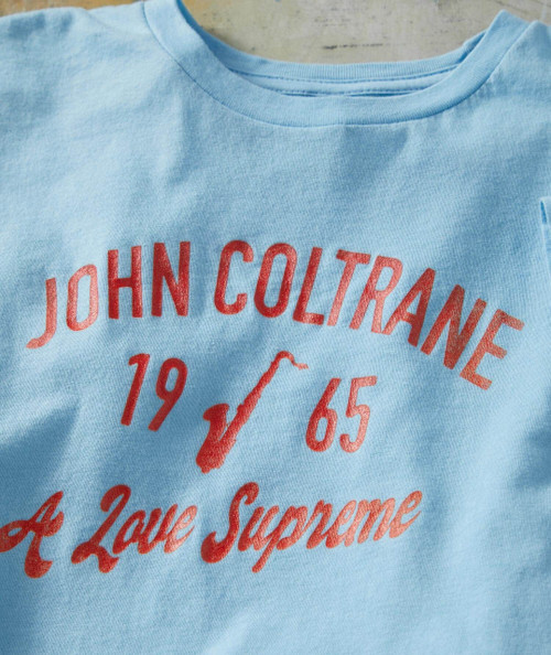 A Love Supreme, light blue T-shirt with red printed text and graphics related to jazz legend John Coltrane and his iconic album.
