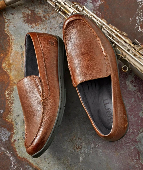 Slim's Stop shoes, brown leather loafers with textured finish and black interior, placed next to a saxophone on a rustic surface.