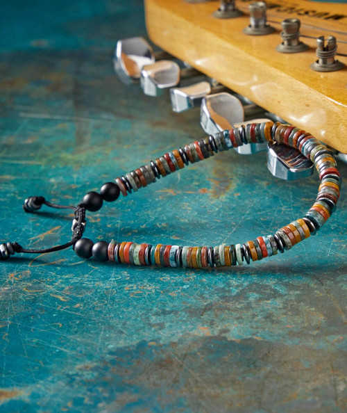 Good Picken's, colorful beaded jewelry necklace with black beads in front of a wooden guitar on a textured green surface.