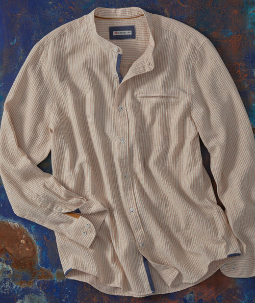 Drifting, a beige striped button-up shirt with a single chest pocket, spread out on a textured blue and rust-colored background.