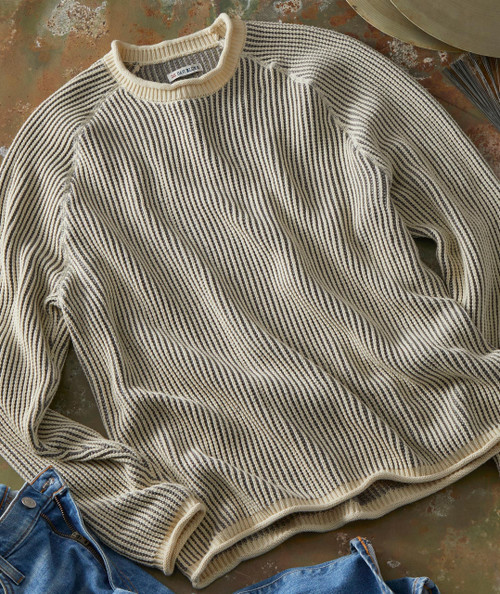 Groove's Groove, striped beige and black knitted sweater laid flat on a rustic surface with denim jeans nearby.