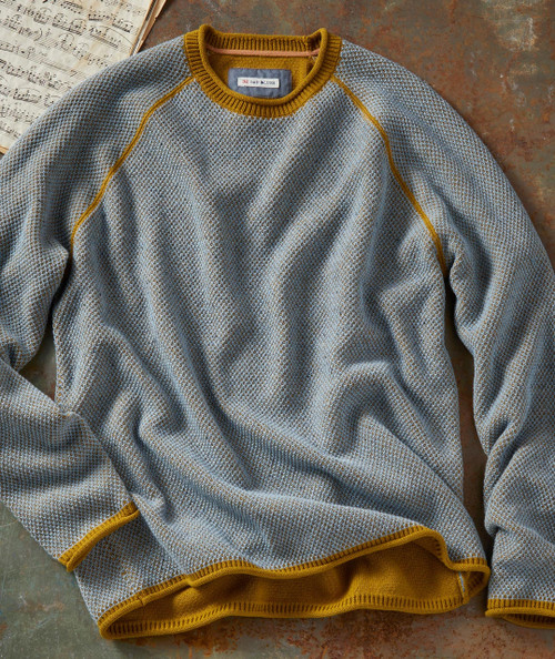 Wild Honey, knitted sweater with a grey and yellow pattern and yellow trim, laid on a rustic surface with sheet music in the background.