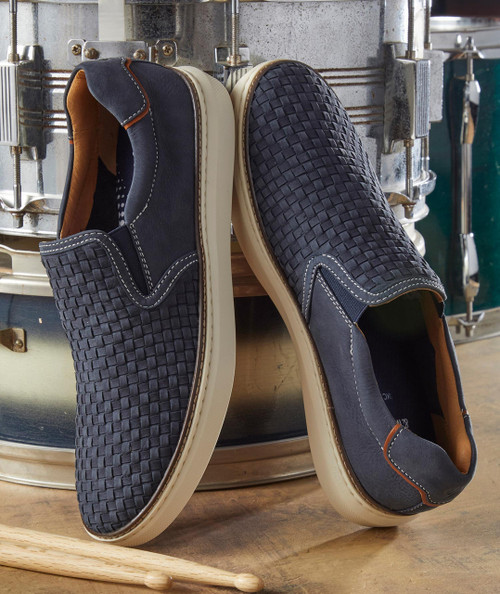 Tanglefoot shoes, fashionable navy blue slip-on sneakers with woven design and white sole, placed near a metallic drum in a workshop setting.