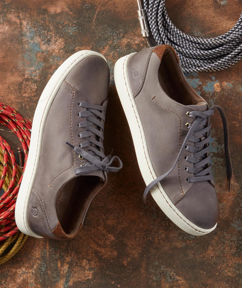 The Stride, stylish grey casual sneakers with brown accents and white soles, paired with climbing ropes and a carabiner on a rustic surface.