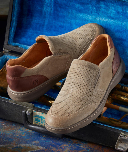 Dig A Hole, pair of men's slip-on shoes with perforated suede uppers and leather accents, placed inside an open vintage blue suitcase with a textured handle.