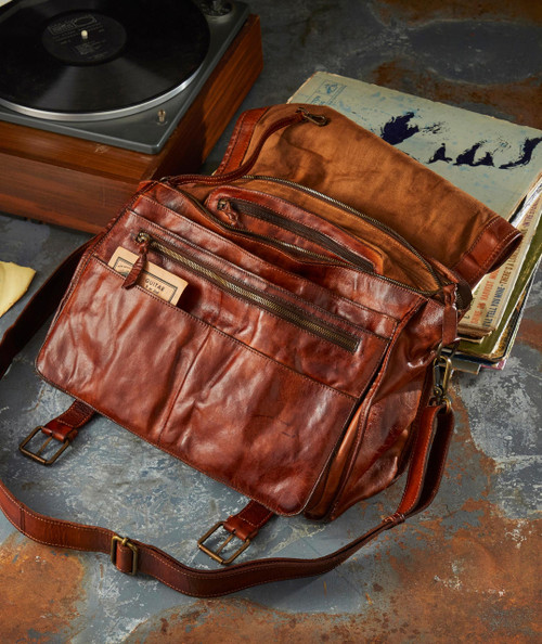 Trick Bag, vintage brown leather bag with multiple zippered compartments on a rustic floor with vinyl record player and books.