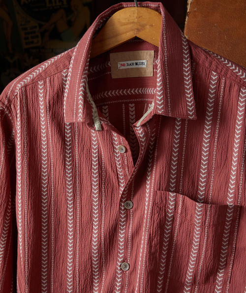 Red Arrow, vintage red patterned button-up shirt with white vertical stripes and herringbone design, hanging on a wooden hanger.