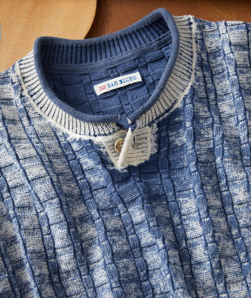 Drifting Blues, close-up of a patterned knitted sweater with a high collar and button detail, featuring a mix of cream and blue colors.