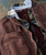 32 Bar Blues Divided Highway, close-up of layered clothing including a brown jacket, plaid shirt, and a graphic t-shirt.