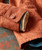 32 Bar Blues Please Do Something, close-up of a worn orange jacket sleeve with a tan button and layered cuffs, on a textured surface.