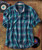 32 Bar Blues Cool Cool Daddy, a blue and green plaid short-sleeve shirt with a front pocket, laid flat on a textured surface alongside vinyl records and a turntable.