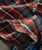 32 Bar Blues Goody Good Good Stuff, a close-up image of a plaid flannel shirt with a pattern of orange, black, white, and blue lines, showcasing its soft fabric and detailed stitching.