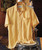 32 Bar Blues Sunshower, yellow short-sleeve button-up shirt hanging on a wooden hanger against a brick wall background.