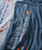 32 Bar Blues Play It Forward, close-up image of fabric with printed guitar neck graphic and logo in orange and white lettering on navy and gray t-shirts.