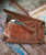 32 Bar Blues Only In It For The Money, Vintage leather clutch bag with zipper pocket and flap closure, placed on a wooden surface with scattered papers.