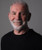 32 Bar Blues Jeff Fasano - Americana Portrait Sessions, image of Jeff Fasano smiling with gray hair and beard, wearing a black shirt against a gray background.