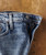 32 Bar Blues That Right There, close-up image of a pair of classic blue denim jeans with a partially unzipped fly on a wooden surface.