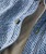 32 Bar Blues Jumpy Blues, close-up of a textured blue and white fabric shirt with green and white buttons and orange stitching.