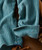 32 Bar Blues Smile Like That, close-up of a pair of vintage turquoise corduroy pants with vertical ridges and a folded cuff, lying on a wooden surface.