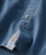 32 Bar Blues Blue's Good Groove, close-up of a blue button and orange stitching on a denim shirt with a small musical note logo.