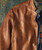 32 Bar Blues Flyjack leather jacket, close-up of brown textured leather with green inner lining and layered clothing underneath.