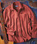 Better All The Time, a long-sleeved, button-up casual shirt in reddish-brown with a single chest pocket, laid flat on a textured, multicolored surface.