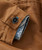 Better Ways, close-up of a brown jacket cuff showing a black button and detailed stitching with a glimpse of the jacket's inner lining in denim style.