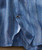 Space Race, a close-up image of a striped blue and multi-colored fabric shirt with a visible button and partial open cuff.